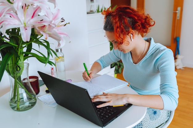 Portrait redhaired teenage girl sitting at table in room using computer