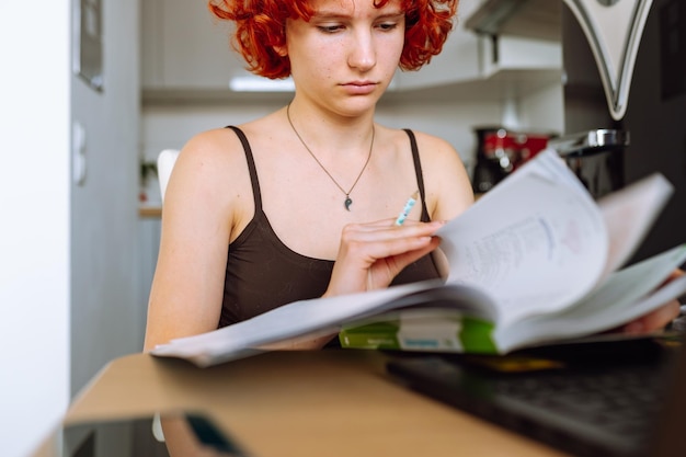 Photo portrait redhaired teenage girl sitting at table in room using computer