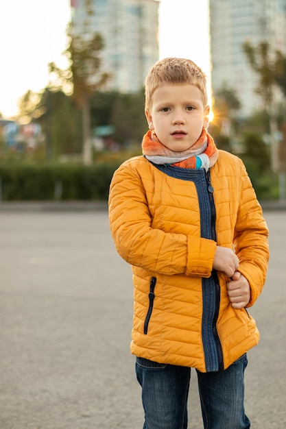 Portrait of redhaired teenager boy in yellow jacket looking at camera and walking at sunset