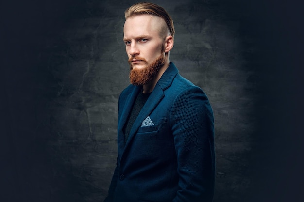 Portrait of redhead bearded hipster male dressed in a blue jacket over grey background.