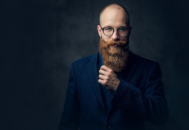 Portrait of redhead bearded male in eyeglasses dressed in an elegant wool suit over grey background.