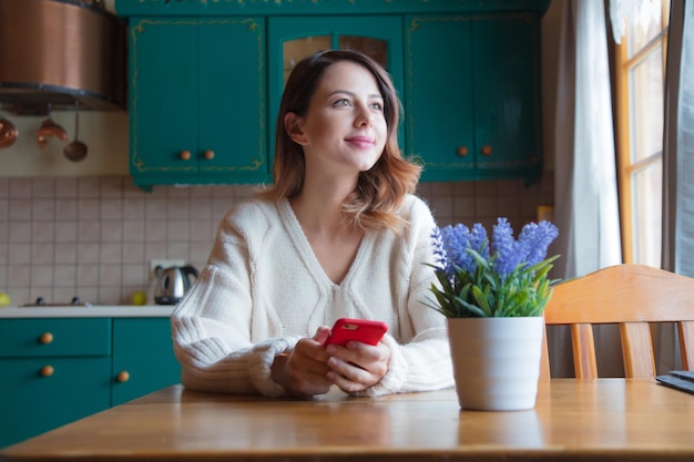 portrait of redhead girl with mobile phone sitting at table in kitchen.