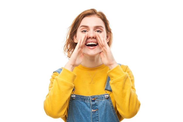 Portrait of redhead young woman screaming into her palms on white studio background Important information news concept