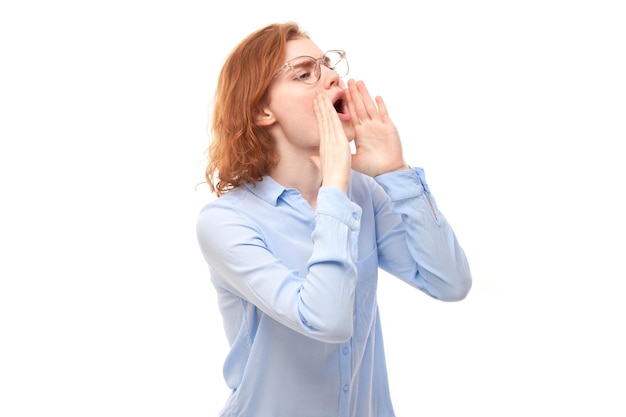 Portrait of redhead young woman screaming into her palms on white studio background Important information news concept