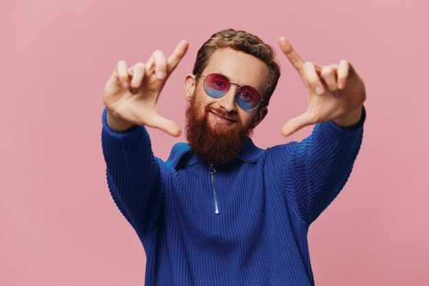 Photo portrait of a redheaded man wearing sunglasses smiling and dancing listening to music on a pink background hipster with a beard happiness finger pointing