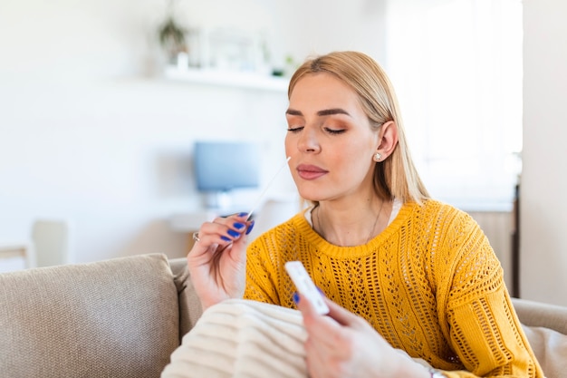 Portrait of relaxed young woman taking a Self-swabbing home tests for COVID-19 at home with Antigen kit. Introducing nasal stick to check the infection of Coronavirus. Quarantine, pandemic.