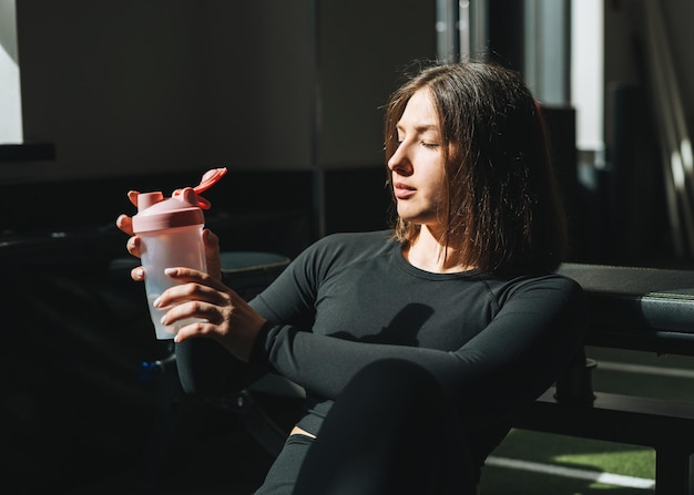 Photo portrait of resting young brunette woman in sport active wear drinking water in the fitness club