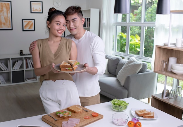 Portrait of romantic Asian couple is cooking on kitchen and looking at camera Happy young man and young woman are having fun together while prepare food Couple lifestyle concept