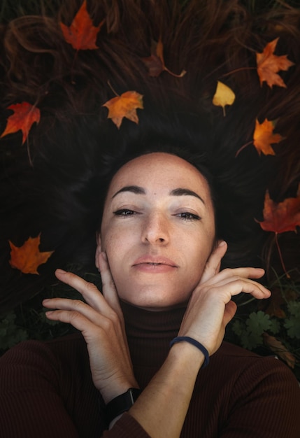 Portrait of sad beautiful young woman lying on the ground of an autumn forest with colorful maple leaves Concept blue monday