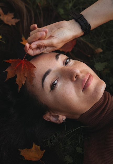 Portrait of sad beautiful young woman lying on the ground of an autumn forest with colorful maple leaves Concept blue monday