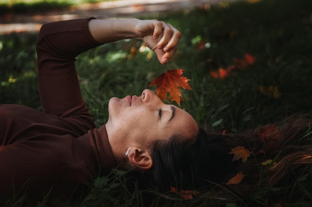 Portrait of sad beautiful young woman lying on the ground of an autumn forest with colorful maple leaves Concept blue monday