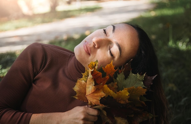 Portrait of sad beautiful young woman lying on the ground of an autumn forest with colorful maple leaves Concept blue monday