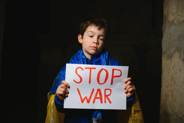 Portrait sad boy protesting war raises banner with inscription Stop War at blue yellow flag of country Ukraine Call to stop war child against war crisis in Ukraine