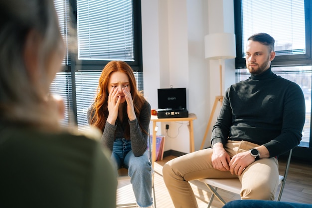 Portrait of sad crying young woman sharing problem sitting in circle during group therapy session. Depressed female telling about mental problem covers face with hands.