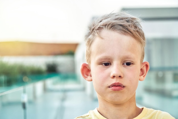 Portrait of sad little boy with blond hair on blurred background