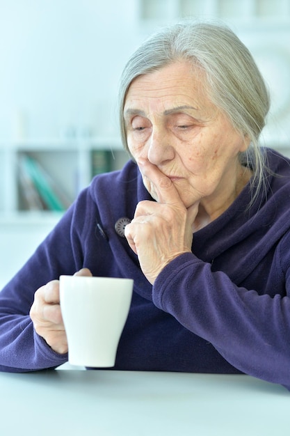 Portrait of a sad old woman drinking tea