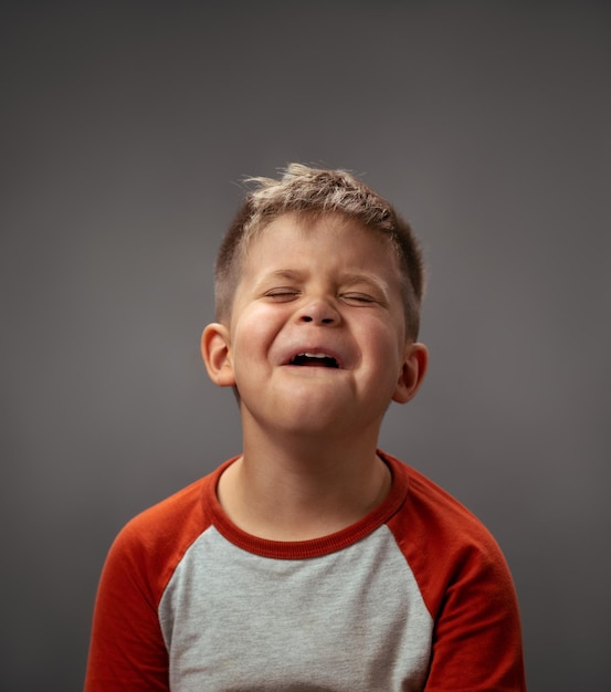 Portrait of a sad pretending cry little boy isolated on grey background fake emotions human emotions...