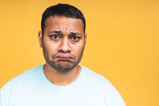 Portrait of sad updet or bored african american black indian young man standing and looking at camera with dissatisfied sadness face. Indoor studio shot, isolated on yellow background.