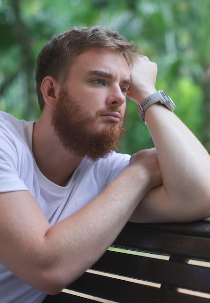 Portrait of sad upset frustrated young man pensive thoughtful guy sit on bench in park and dreaming