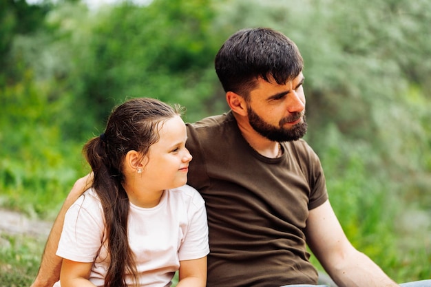 Portrait of satisfied family sitting on picnic in forest around trees bushes Happy father embracing little daughter