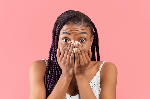 Portrait of scared young african american lady covering her face with hands over pink studio