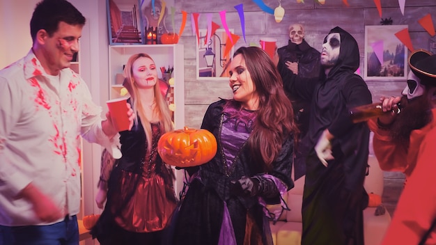 Portrait of scary witch dancing at halloween party holding a jack-o-lantern pumpkin in hands.