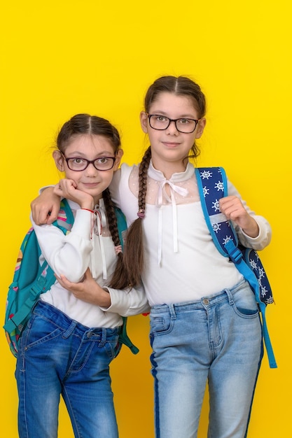 Portrait of school girl Girls sisters in glasses and school bag on Yellow