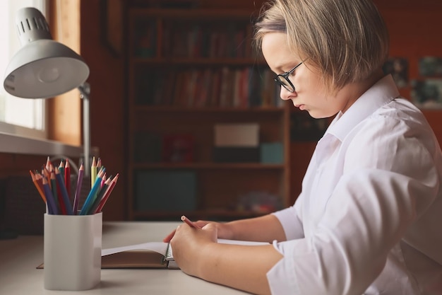 Portrait of the schoolgirl siting at the table indoors and doing her homework The girl does homework at home Distance learning Lessons homework education