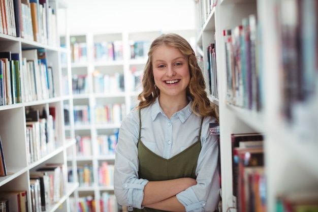 Portrait of schoolgirl standing with arms crossed in library