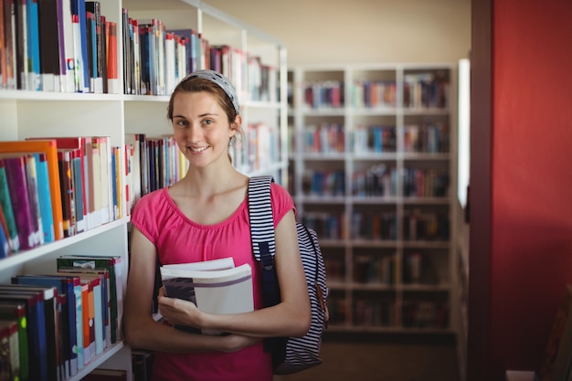 Portrait of schoolgirl standing with books in library