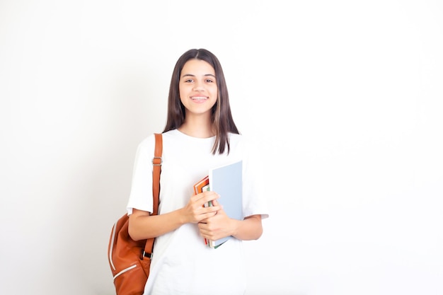 Portrait of a schoolgirl with a backpack and books The student girl looks into the camera and smiles White background A place for text Academic year semester exam Science