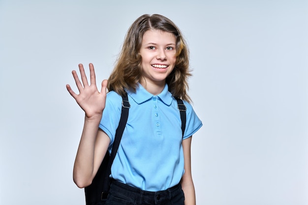 Portrait of schoolgirl with backpack looking at camera waving hello or goodbye