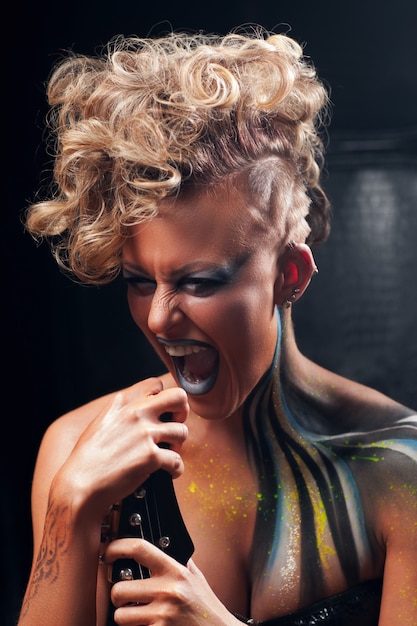 Portrait screaming punk woman with body art and guitar