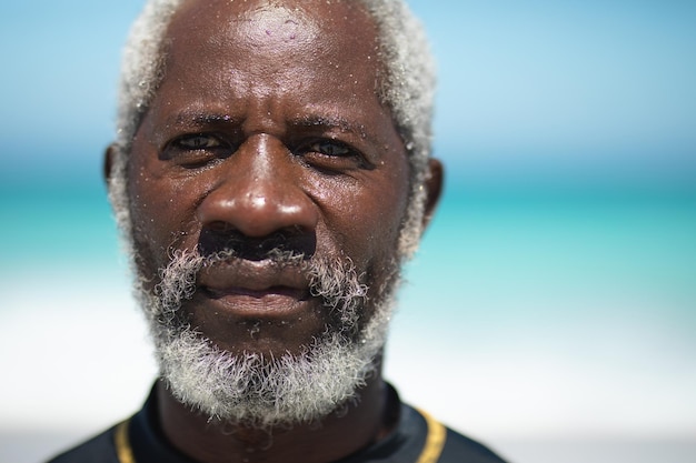 Portrait of a senior African American man on a beach in the sun, looking straight to camera, with blue sky and sea in the background