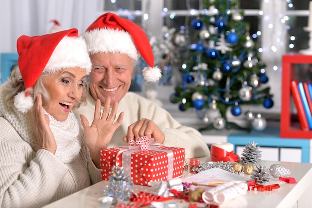 Portrait of senior couple celebrating Christmas, sitting at the table with present