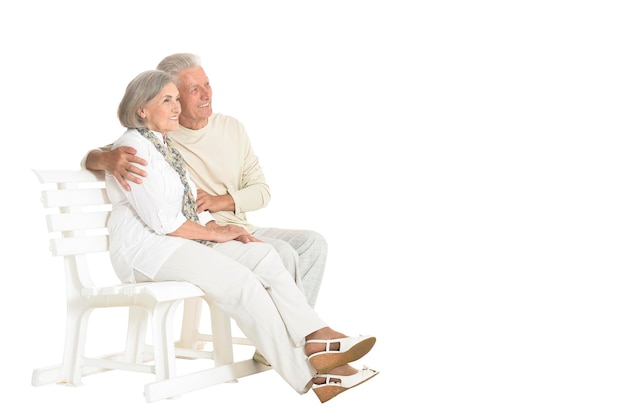 Portrait of senior couple sitting on bench on white background