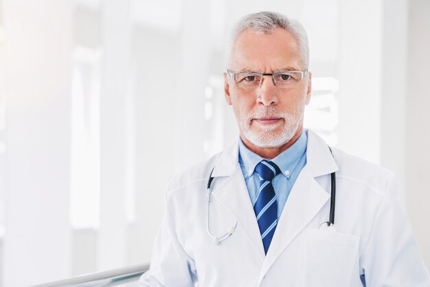 Portrait of senior doctor working at hospital while standing in hall