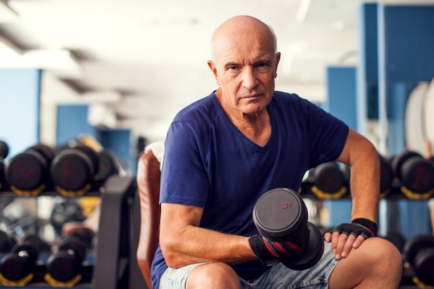 A portrait of senior man in the gym training with dumbbells. People, health and lifestyle concept