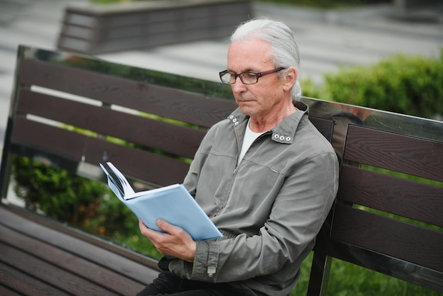 Portrait of senior man reading on bench during summer day