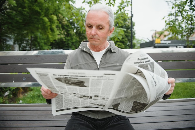 Portrait of senior man reading on bench during summer day