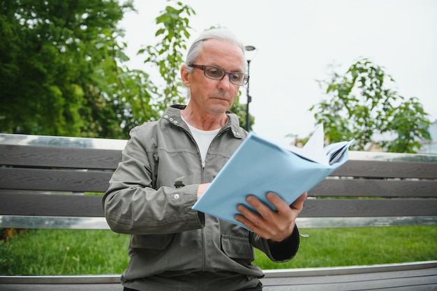 Portrait of senior man reading on bench during summer day