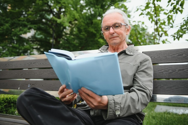 Portrait of senior man reading on bench during summer day