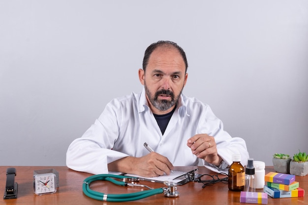 Portrait of senior mature doctor pleasant professional in white coat sitting at table