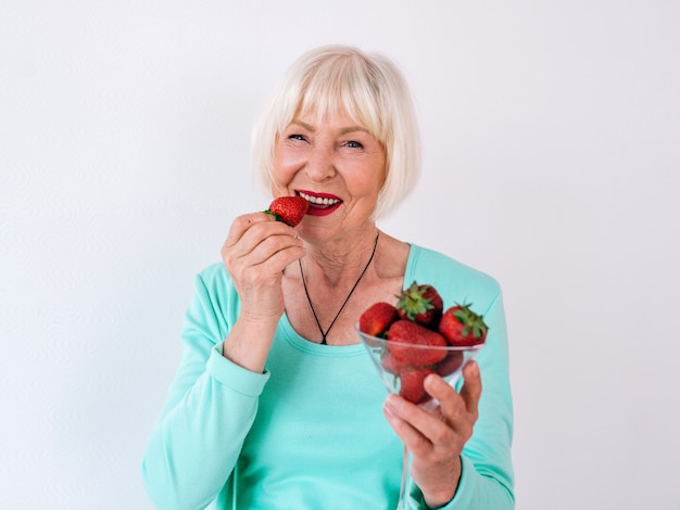 Portrait of senior old stylish cheerful woman in  turquoise clothes eating strawberries