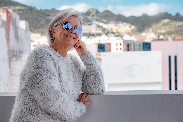 Portrait of senior woman smiling and looking at city landscape Face of a happy senior woman wearing blue reflective sunglasses outdoors Relaxed retired woman with gray hair