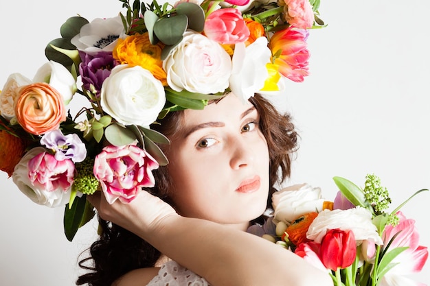 The portrait of a sensitive girl with a wreath on her head holding a bouquet of flowers, closeup