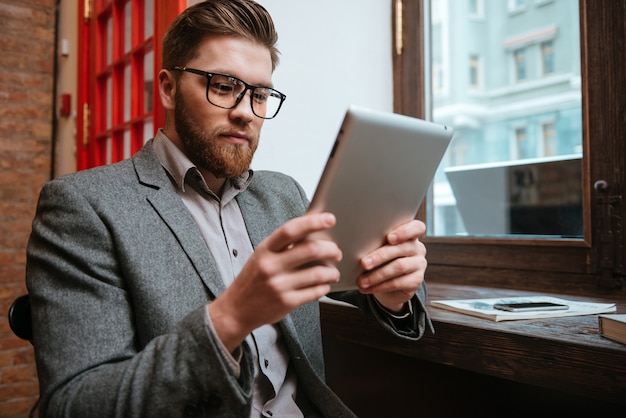 Portrait of serious businessman sitting at the table and holding tablet computer