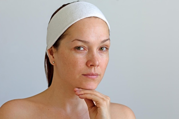 Portrait of serious caucasian middle aged woman without make up with band on head holding chin by ha