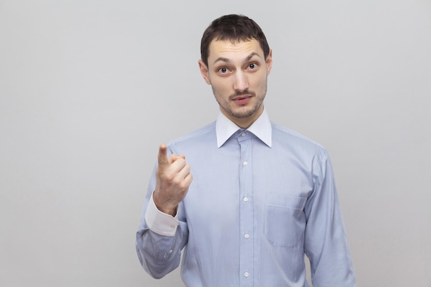 Portrait of serious handsome bristle businessman in classic light blue shirt standing and looking at camera with warning sign. indoor studio shot, isolated on grey background copyspace.