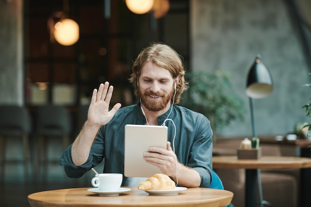 Portrait of serious modern guy with beard sitting at round table in loft cafe and calling by mobile